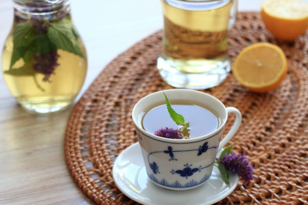 Ceașcă elegantă cu ceai de isop pe masă alăruri de lămâie, o carafa cu limonadă și un pahar